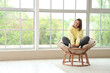 © Pixel-Shot - Young woman sitting in cocoon chair near window at home