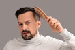 © Pixel-Shot - Worried young man with hair loss problem brushing on grey background, closeup