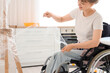 © Pixel-Shot - Young woman in wheelchair wrapping lamp during repair at home