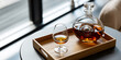 © ismail - Glass bottle of brown liquor and glass on wooden tray on table by window