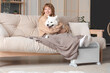 © Pixel-Shot - Young woman with blanket and Samoyed dog on sofa warming near radiator at home