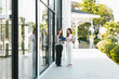 © artitwpd - Two professionals discuss documents outside a modern glass office building, standing on a sunny walkway bordered by greenery.