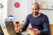 © Westend61 - Smiling man shopping online with credit card at home workspace