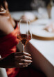 © dreamalittledream - Elegant fine dining: close-up of woman in red dress holding wine glass for luxury lifestyle and hospitality themes.A sophisticated and alluring detail shot of a celebratory moment