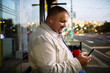 © Marko Geber - Smiling man using smartphone at city bus stop at dusk