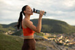 © Home-stock - Woman drinking water in nature after morning cardio, running or yoga, standing on hilltop viewing city and hills. Hydration for workout recovery