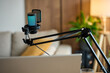 © Lazy_Bear - Microphone with pop filter on boom arm and laptop in home interior with sofa and plant in background. Concept of podcast recording, streaming setup and audio content creation