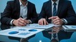 © Hi_depari - Two business professionals analyzing financial reports on a reflective glass table in a corporate setting