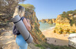 © Angelov - Woman standing confidently on a coastal cliff with a yoga mat, embracing a healthy and balanced lifestyle while enjoying outdoor wellness with the ocean and blue sky in the background