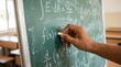 © tonstock - Close up of a hand writing complex mathematical formulas and physics equations on a green chalkboard in a classroom.