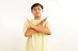 © Wayan - Asian man with a serious expression and arms crossed in a rejection gesture, isolated on a clean white background, symbolizing refusal and denial
