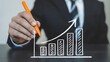 © Adobe 2.0 - Hand holding orange pen drawing an upward trend bar graph symbolizing business growth and success