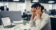 © Georgiy - Stressed woman sitting at desk in office. Employee having headache or burnout while working on laptop. Professional pressure and workplace mental health struggle for corporate career.