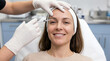 © Facundo - Smiling woman wearing a headband receiving a cosmetic facial injection in a clinic.