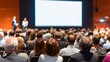 © Iuliia - Audience at a conference listening to speakers on stage with a large blank screen. Business meeting and education concept for presentation.