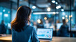 © Kateryna - Faceless woman from behind in a bright creative office workspace seated at a clean desk with a laptop open and displaying a marketing analytics interface colleagues visible