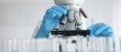 © rogerphoto - Female scientist wearing protective equipment checking microscope, analyzing blue test tubes in modern laboratory research setting. Medicine, healthcare and science concept