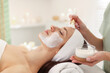 © New Africa - Beautician applying moisturizing mask with brush onto woman's face indoors, closeup
