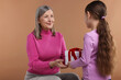 © New Africa - Little girl greeting her grandmother with gift on dark beige background