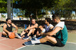 © AntonioDiaz - Four young men sitting on a basketball court, taking a break, drinking water, and having a conversation