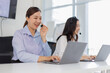 © David - Cheerful women collaborating in a bright, modern office, wearing headsets while engaging with their laptops, representing productivity and the importance of communication and teamwork.