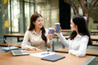 © Nuttapong punna - Two businesswomen celebrating success during an outdoor coffee meeting with laptop and documents, representing teamwork, startup collaboration