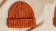 © Via - Close-up shot of an orange knit cap on a white fabric background, partial view of another cap