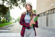 © wavebreak3 - Female student standing on campus wearing beanie and over-ear headphones holding spiral notebooks