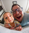 © phpetrunina14 - Playful father and baby selfie on bed at home.