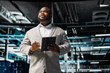 © DC Studio - Engineer in server room overseeing mainframes gear used for managing databases. African american man in data center establishment doing checkup on rackmounts storing information