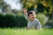 © Anatolii Rymarchuk - Happy baby waving hello while sitting on a lush green lawn in sunlight
