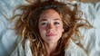 © svastix - A joyful close-up portrait of a young woman with wavy hair, radiating happiness and warmth, surrounded by soft, inviting bedding that adds to her allure.
