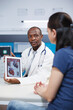 © DC Studio - African American doctor grasping tablet showing heart radiography to woman explaining medication treatment during an appointment in hospital office. Physician describing the diagnosis to patient.