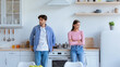 © Prostock-studio - A couple stands in a kitchen arguing. The man has his arms at his sides, wearing a blue shirt. The woman crosses her arms, dressed in a pink sweater. They face different directions, showing tension.