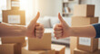 © KAMRAN - Close up of couple hands showing thumbs up against moving boxes perfect for real estate property goal