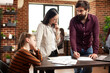 © DC Studio - Two caucasian male and female colleagues discussing with financial documents on table as bored little girl sits nearby. Woman multitasking with parenting and reviewing data with young man in office.