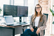 © deagreez - Smiling female software developer at desk with dual monitors and laptop coding in a bright modern office