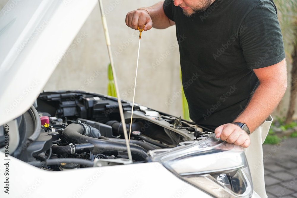 Man checking engine oil level with dipstick under the open car hood ...