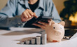 © JK_kyoto - Piggy bank coins calculator laptop person saving money finance investment growth business table indoor technology casual office currency stack counting planning budget financial planning economy
