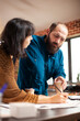 © DC Studio - Bearded man holding coffee cup and providing input during business meeting with female analyst at office desk. Closeup on caucasian coworkers having warm beverage and reviewing financial paperwork.