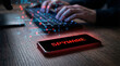 © ViskBx - A smartphone on a desk shows a red 'SPYWARE' warning while a hacker types in the background.