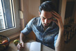 © Teodor Lazarev - Concerned man feeling stressed and having headache while thinking and writing notes in a notebook, managing work or personal challenges at a home working desk