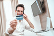 © Teodor Lazarev - Happy man talking on phone, holding credit card for online shopping, making secure payment, enjoying e-commerce services and comfortable remote work in hotel room