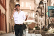 © Teodor Lazarev - Young man smiling, communicating on smartphone, walking in city street expressing happiness and confidence while making a phone call outdoors