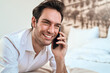 © Teodor Lazarev - Happy smiling man discussing on a smartphone while resting relaxed on the bed in a bright bedroom, holding modern mobile device for communication and connection
