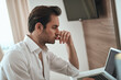 © Teodor Lazarev - Young man concentrating on laptop, experiencing work stress, problem solving, thinking deeply, feeling pressure, and contemplative during remote work indoors