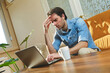 © Teodor Lazarev - Man experiencing severe headache and work stress at home, rubbing his temples while working on a laptop, overwhelmed by remote work pressure and fatigue