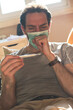 © Teodor Lazarev - Sick man wearing a medical mask and coughing, checking his temperature with a thermometer, staying home while experiencing illness symptoms, feeling unwell and having a fever