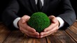 © ZinaZaval - Businessman in a suit holds a green grass sphere on his desk, symbolizing commitment to eco-friendly practices and sustainability