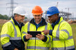 © Md Ikbal - Three construction workers in high-visibility jackets and hard hats review a tablet on a building site
